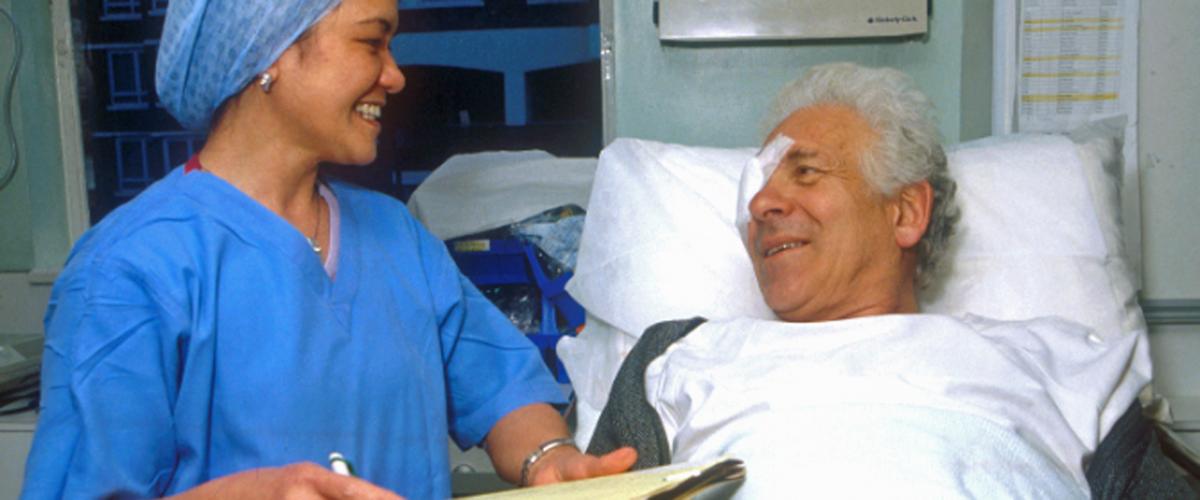 Man on hospital bed with eye patch smiling with a nurse by his side